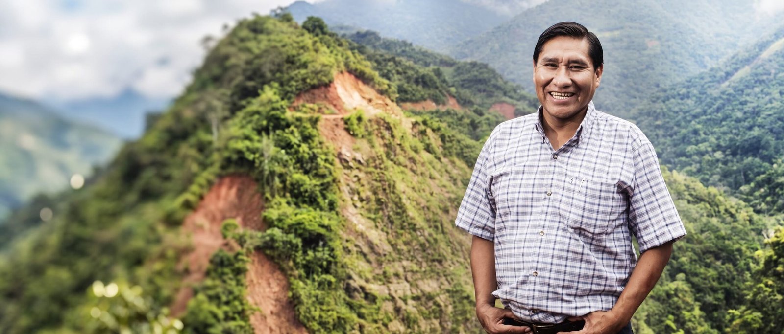 Raúl Mamani, caficultor de Uchuñari Coffee, sonríe de pie frente a las montañas cafetaleras