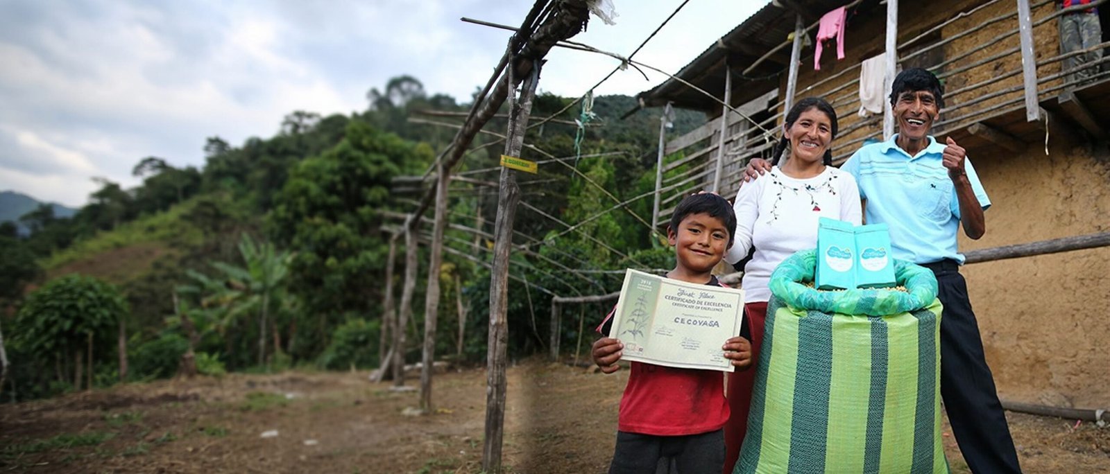 Familia cafetalera con un certificado de excelencia y bolsas de Café de las Nubes sobre un costal de café, frente a su casa de adobe